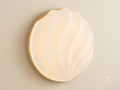 A circular light fixture with a wooden base and a wavy design that mimics the shape of a seashell, featuring a cover that distributes warm light with a subtle, shiny point effect resembling twinkling stars.
