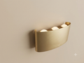 A gold wall sconce with an elegant curved metal design featuring three spherical bulbs that distribute light upwards.