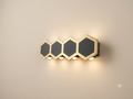 A wall sconce with a geometric design inspired by a honeycomb, consisting of four hexagonal shapes in gold and black.