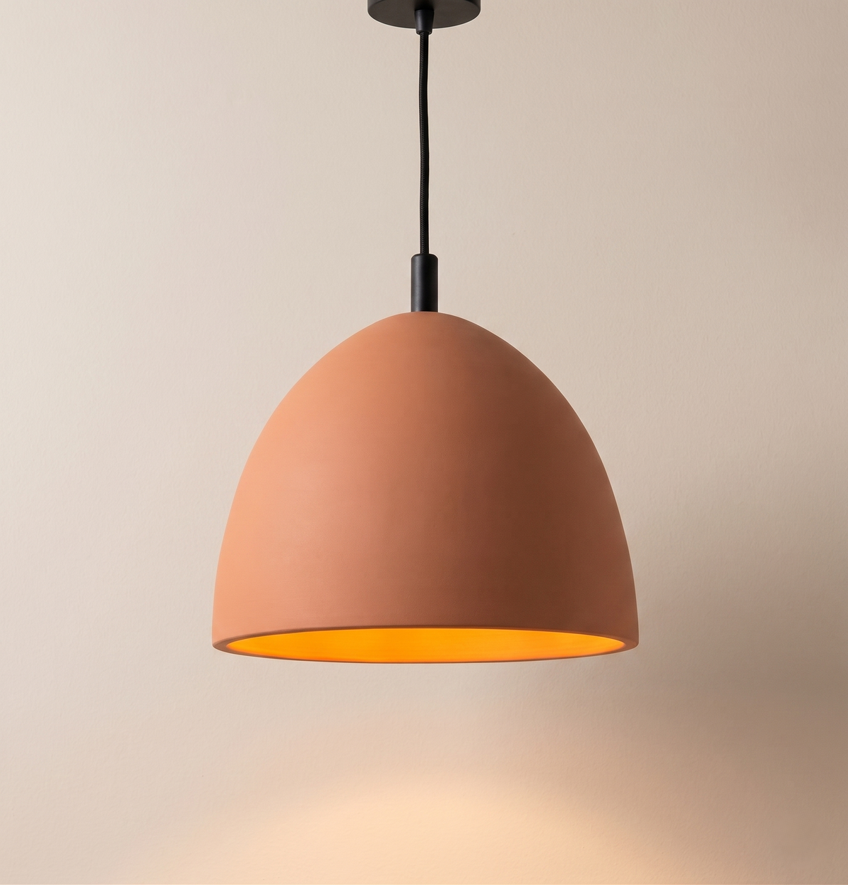 A pendant light with a soft dome design made of glazed terracotta, adding a warm and cozy touch that is perfectly suited to interior spaces with an organic or contemporary character.
