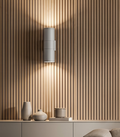 A cylindrical wall lamp that provides up-down lighting and is mounted on a ribbed wooden wall.