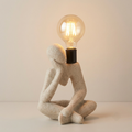 Thinker-pose sculptural lamp with exposed globe bulb
